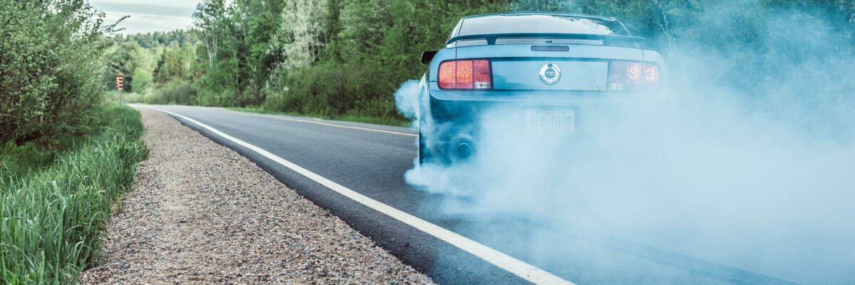 A car releases a plume of smoke as it turns down a road.