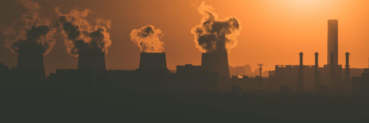 Power plant releasing smoke into an orange hazy sky; the sun is setting.
