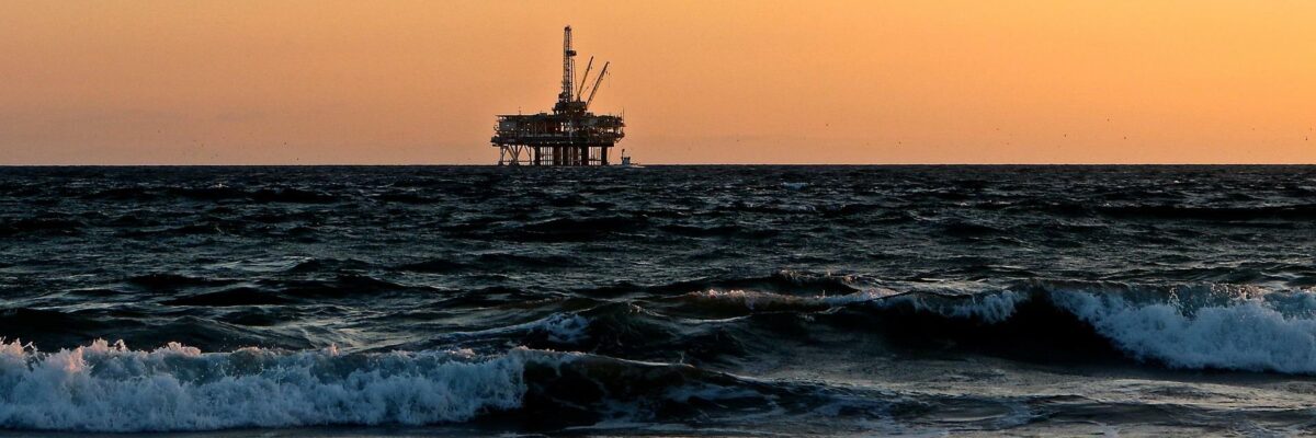 An offshore oil rig in the slightly wavy ocean, backed by a sunset-tinged sky.