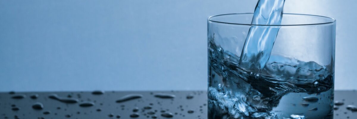 A stream of water is poured into a clear water glass.