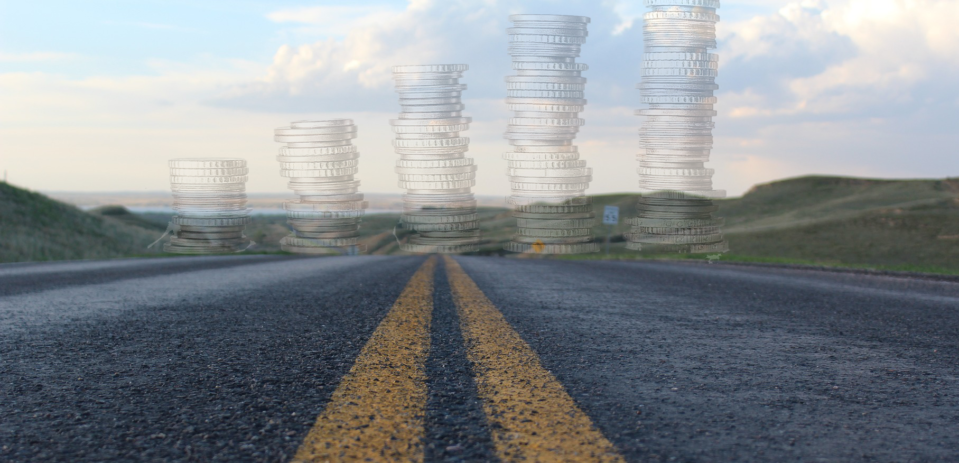 A road viewed from the ground, with yellow lane dividers extending into the distance, meeting a row of five stacks of coins at the horizon, arranged from shortest to tallest