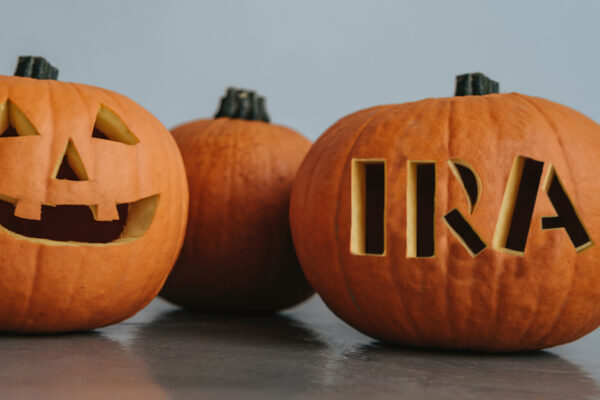 Several large orange pumpkins; one is carved with a jack-o-lantern face, and the other with the letters "IRA"