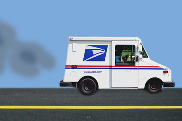 A mail truck drives down the street, releasing exhaust into a blue sky.