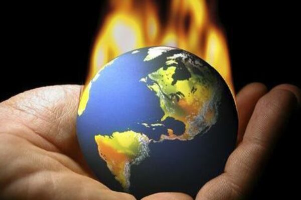A hand cradles planet Earth, which has erupted into flames.
