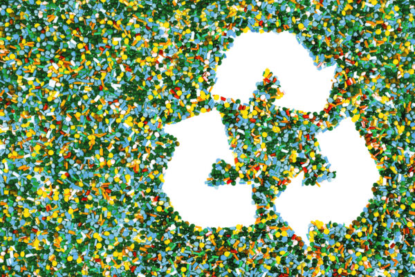 Green, blue, yellow, and red plastic nurdles spread out on a surface; negative space forms the chasing-arrows recycling symbol.