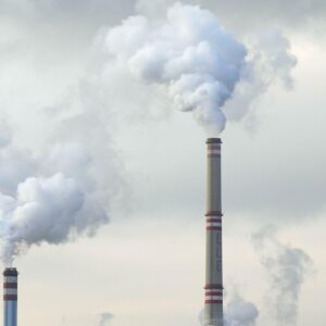 Two think smokestacks releasing large plumes of air pollution into a grey sky.