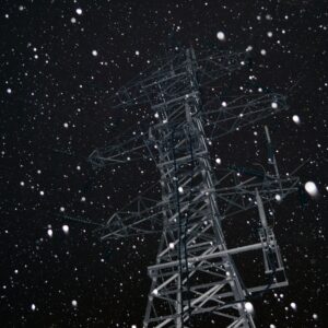 A transmission tower a night surrounding by a flurry of bright white snowflakes standing out against an inky black sky